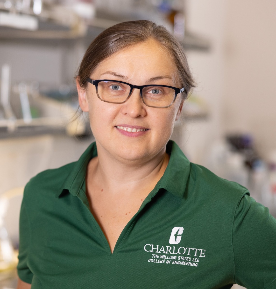 Portrait of Olya Keen wearing a green shirt and glasses in a lab