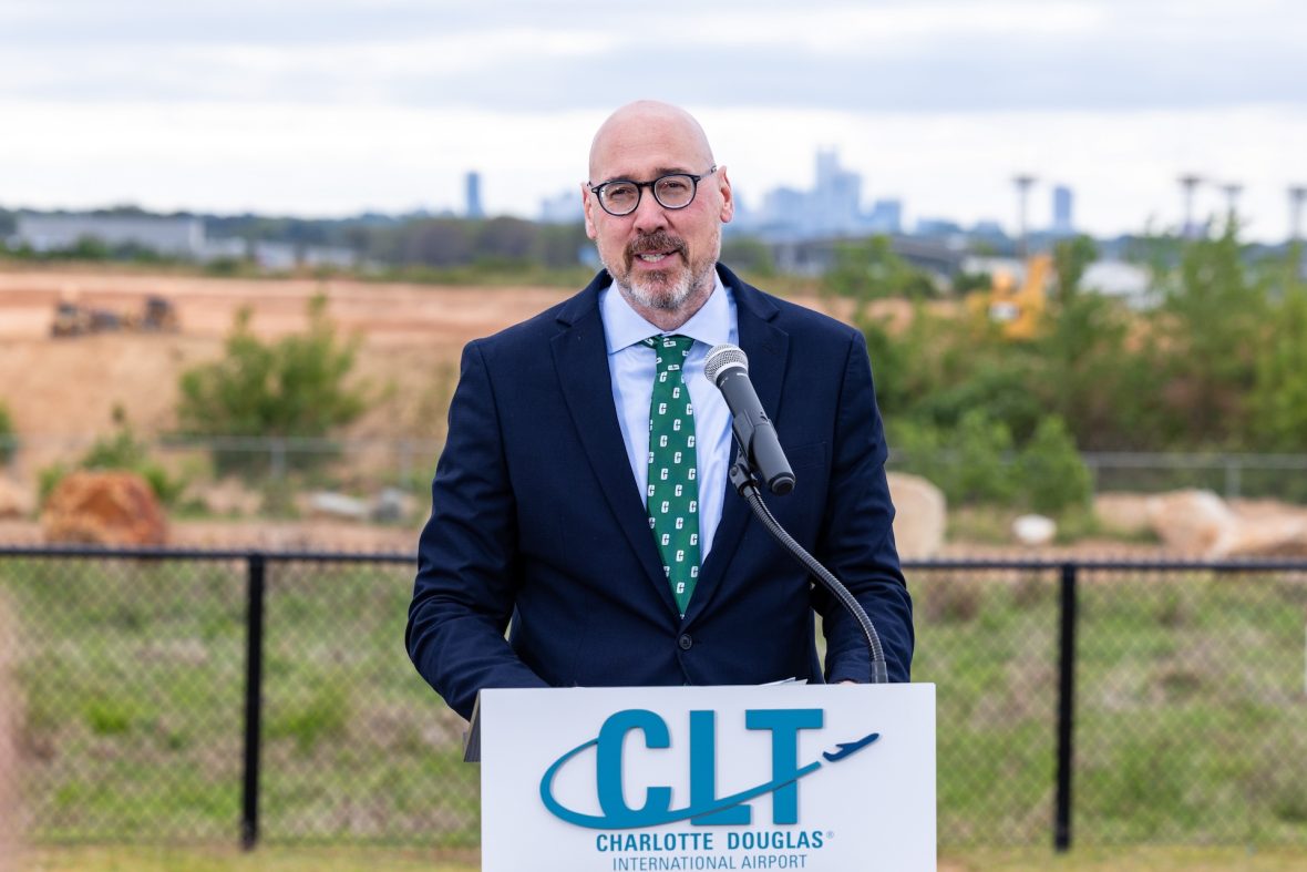 John Daniels speaks from a podium near a runway at Charlotte Douglas International Airport