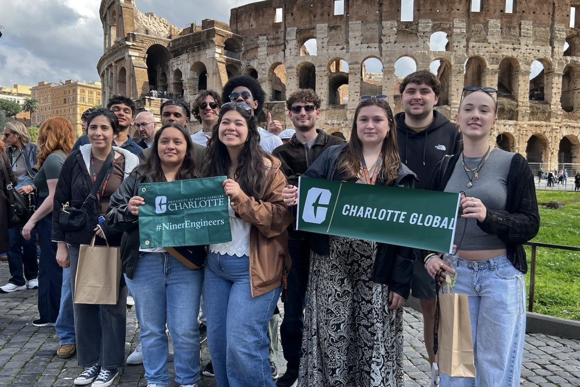 UNC Charlotte engineering students posing while holding green Charlotte Global and Niner Engineers signs