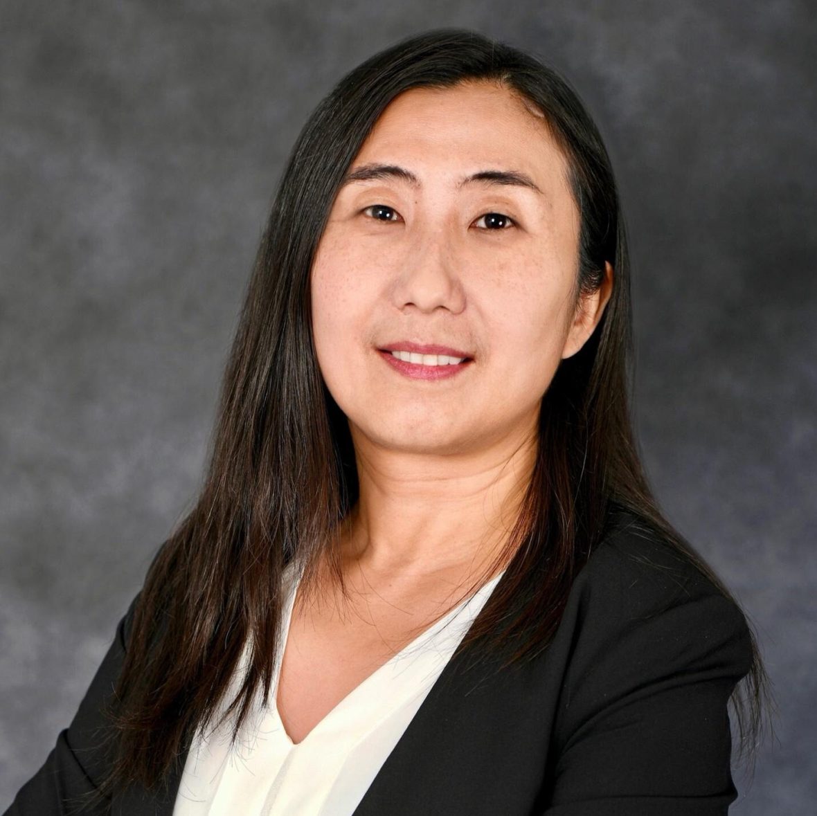 Smiling portrait of Ying Sun with a gray backdrop
