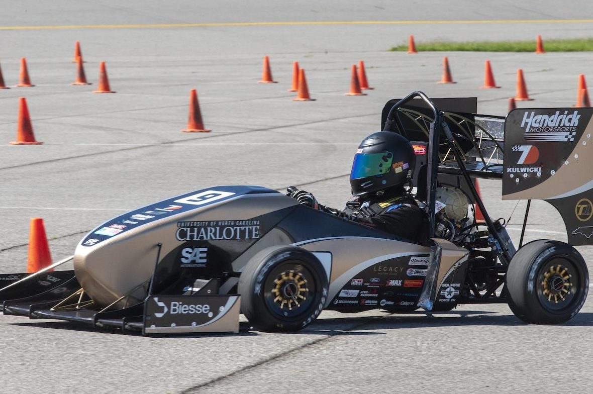 A student FSAE driver drives car on a track with several orange cones