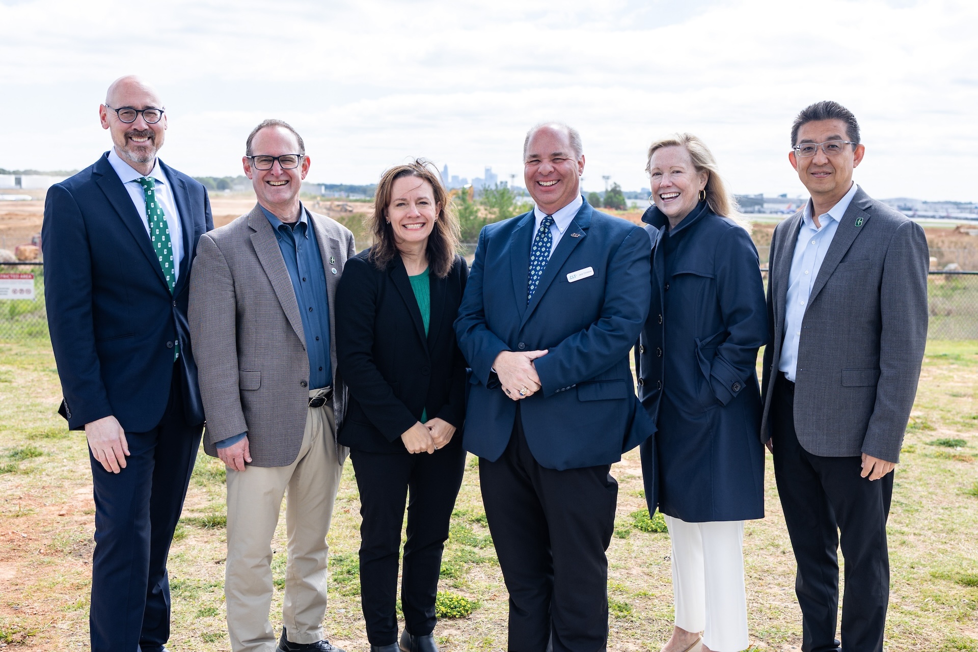 Group of six individuals smiling in a field with the Charlotte skyline in the background