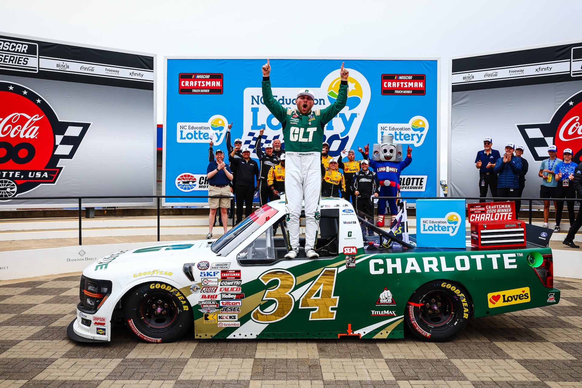 Layne Riggs celebrates NASCAR Craftsman Truck Series win by standing in window of his No. 34 truck. His crew stands behind him.