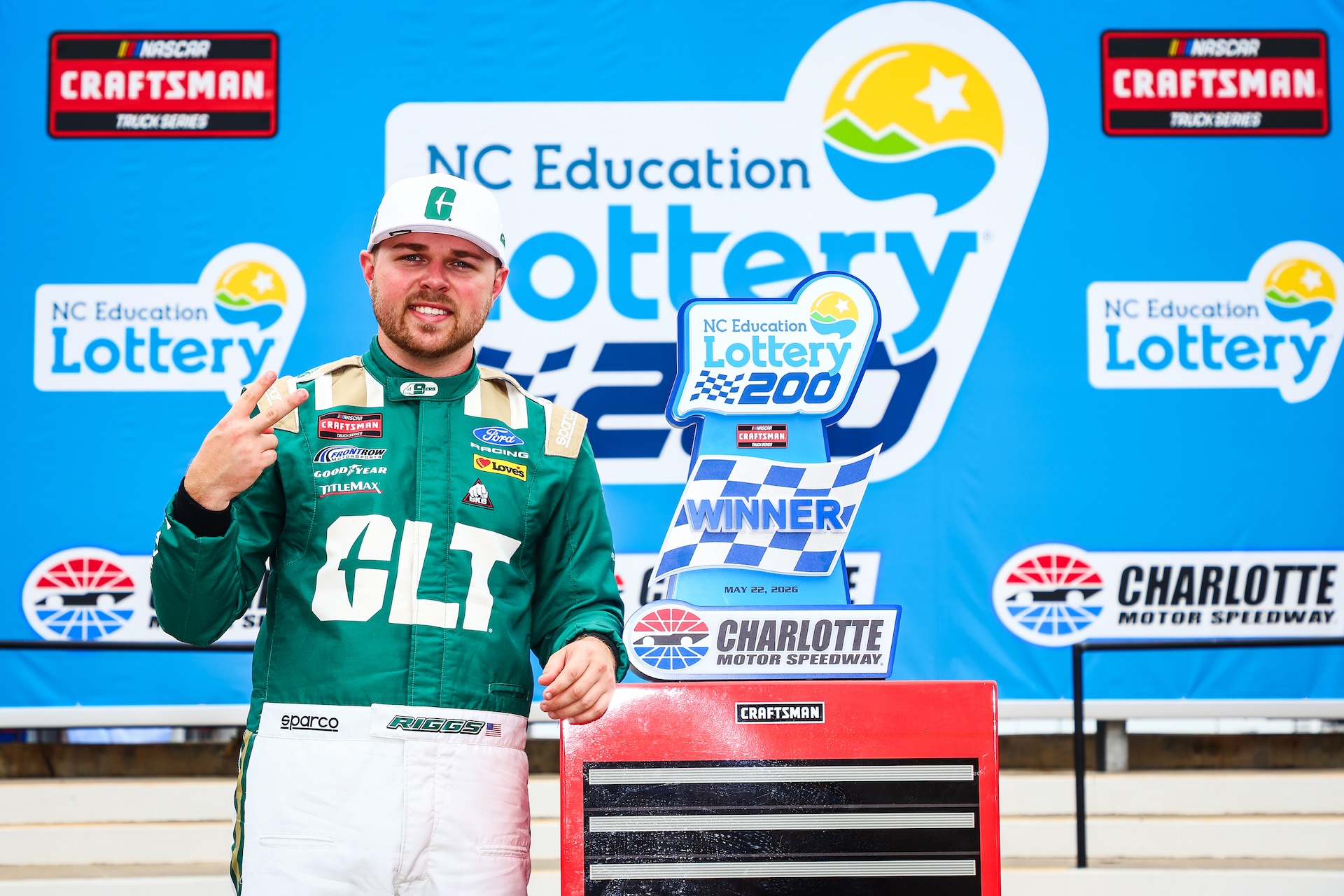 Smiling Layne Riggs stands beside NC Education Lottery 200 trophy in Victory Lane at Charlotte Motor Speedway
