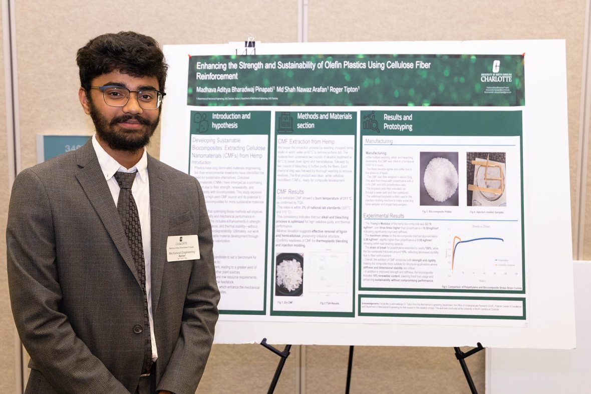 Male student wearing a coat and tie stands next to research project board