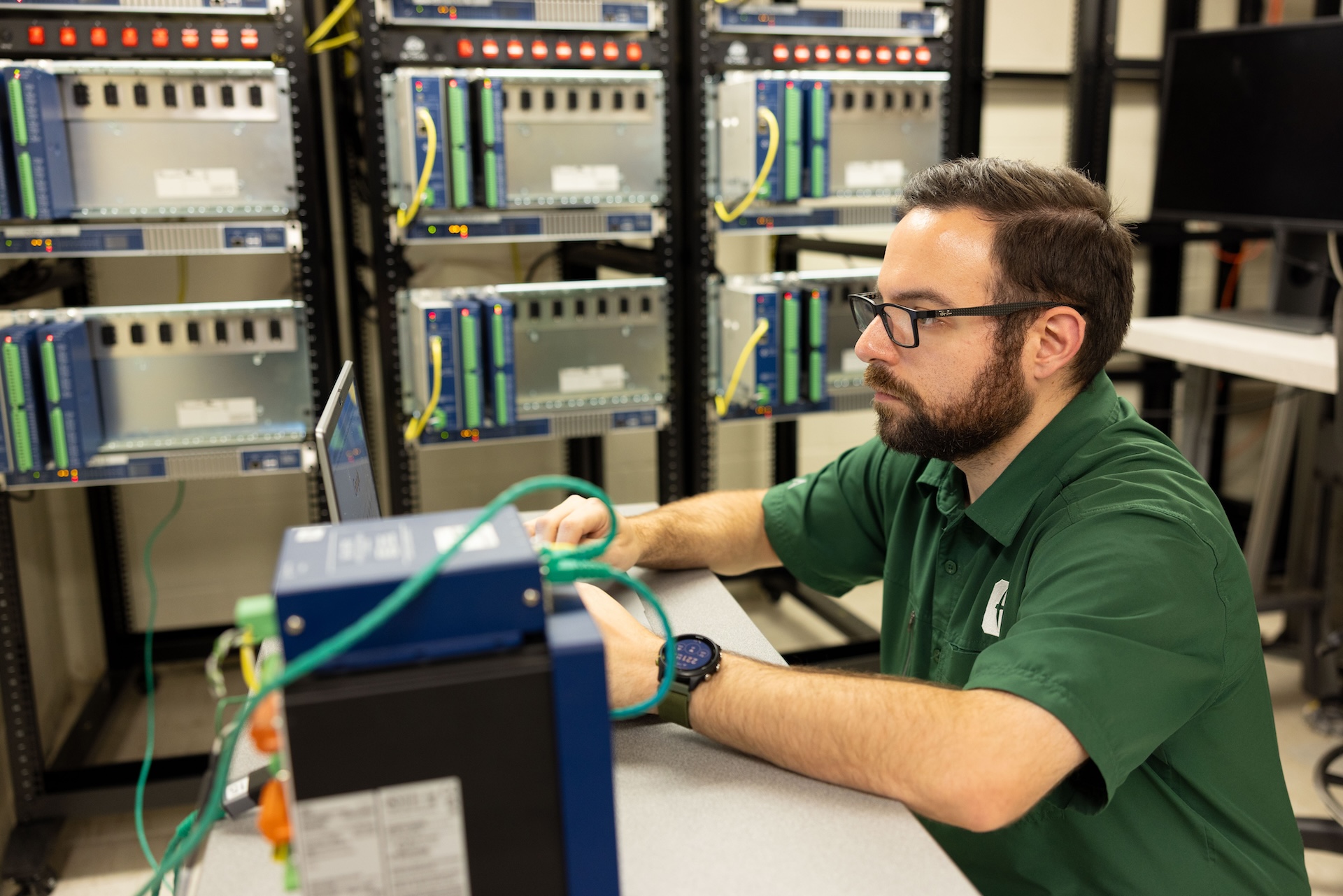 Austin Fifield sits at a table, working on a machine, in a lab
