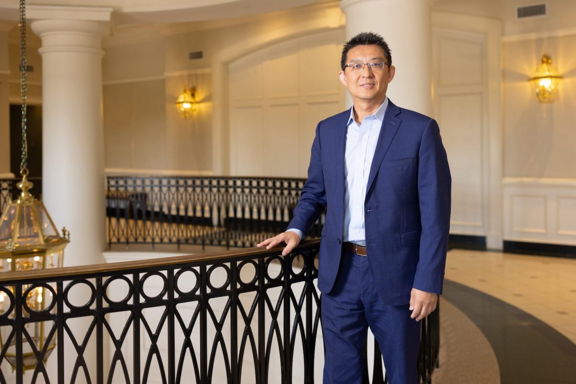 Smiling portrait of Lingguang Song as he stands with hand on rail in the Duke Centennial Building at UNC Charlotte