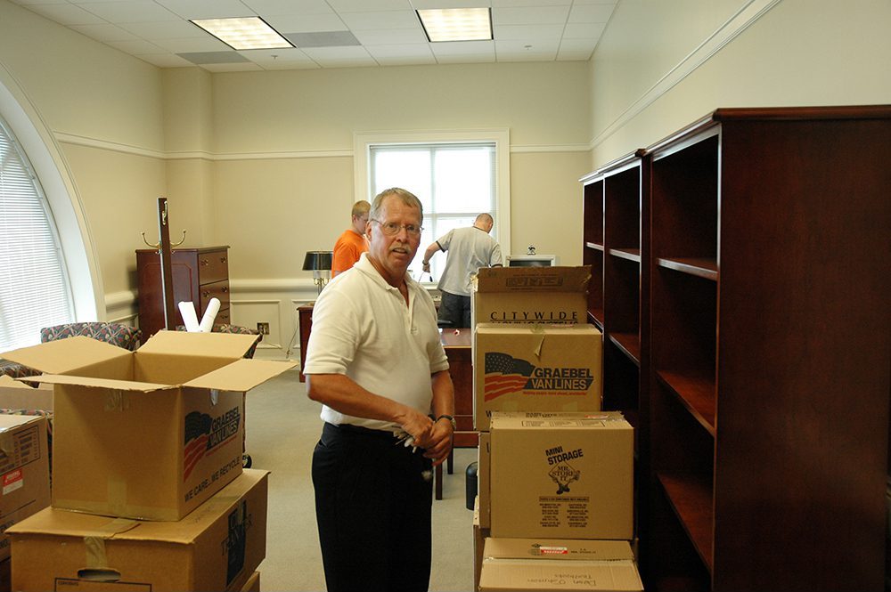 Bob Johnson looks at the camera as he moves into his new office, surrounded by cardboard boxes